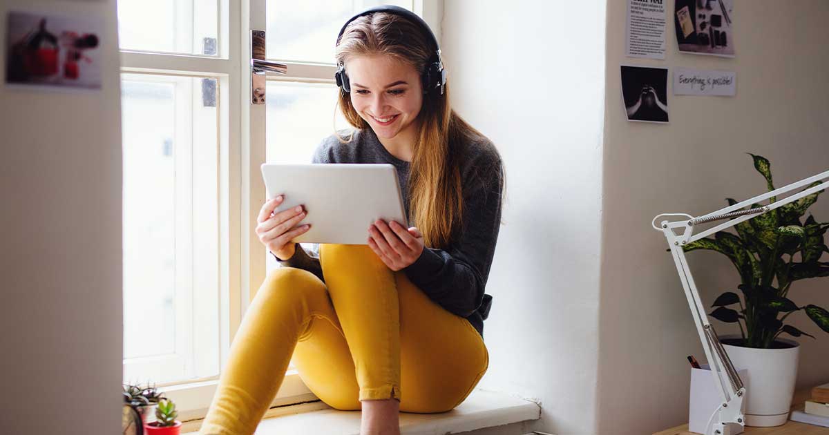 Teenagerin sitzt auf einer Fensterbank und schaut auf Tablet