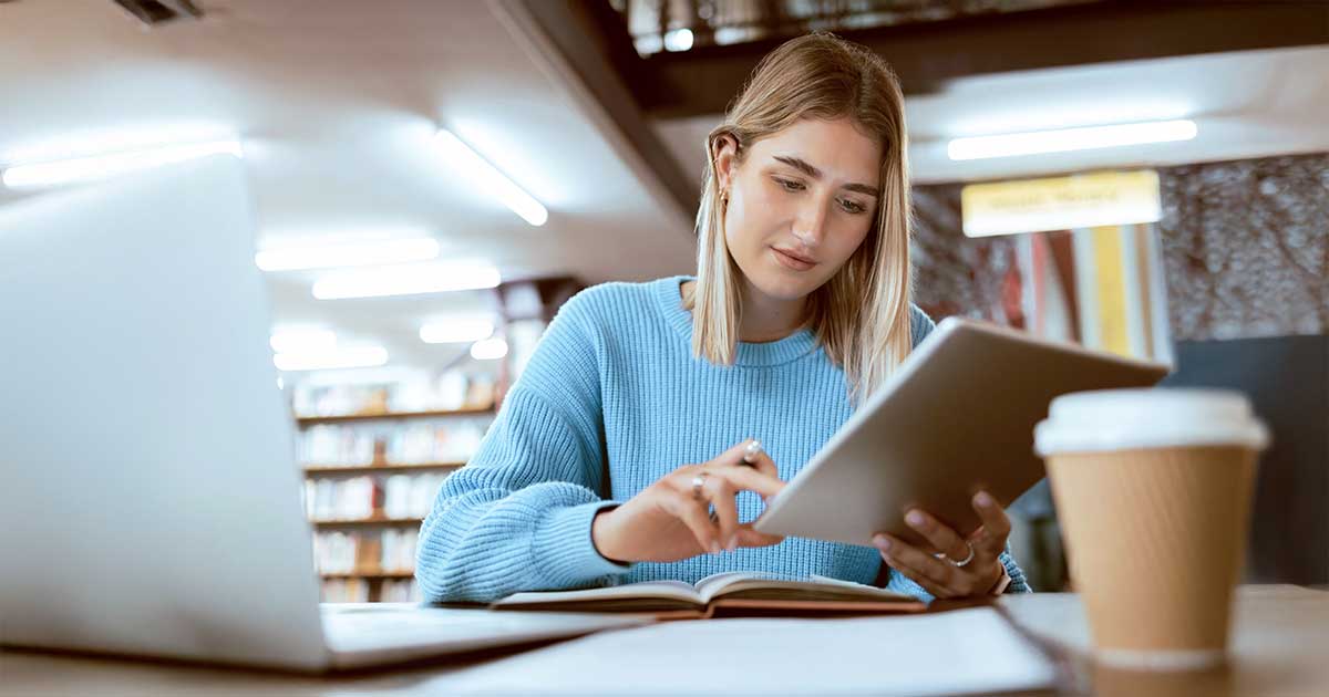 Junge Frau sitzt in Bibliothek und tippt auf Tablet