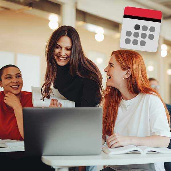 Drei junge Frauen versammeln sich um einen Tisch und schauen auf einen Laptop.