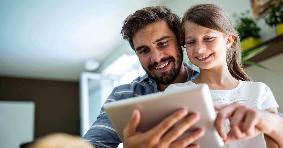 Vater schaut mit Tochter auf Tablet.
