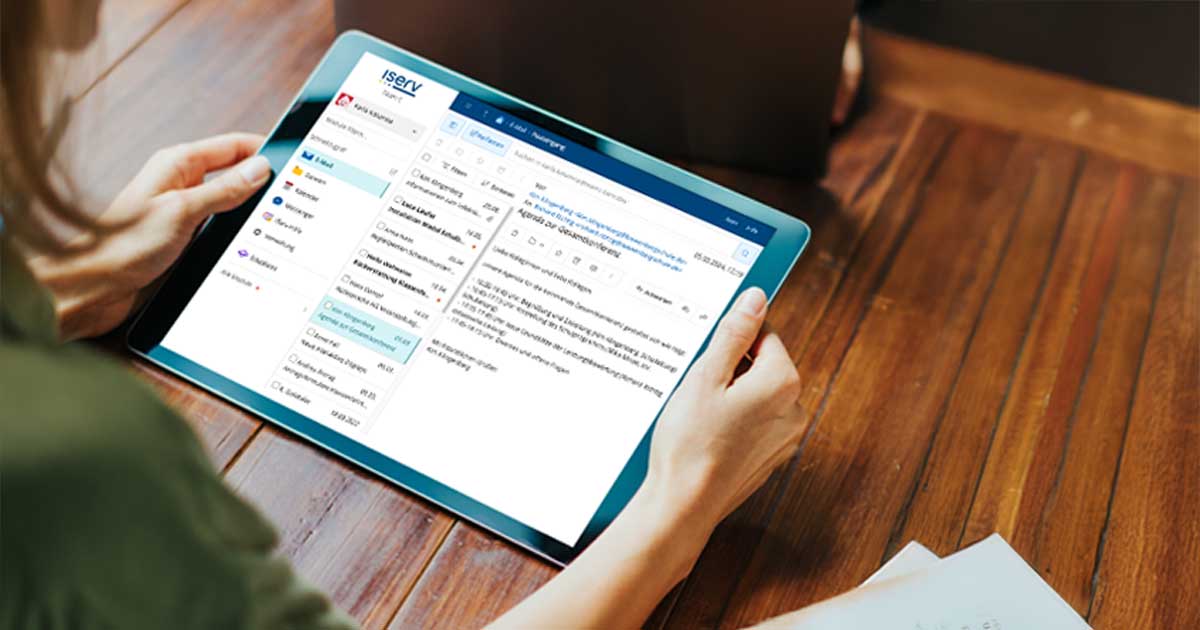 Frau sitzt am Tisch mit Tablet und schaut darauf.