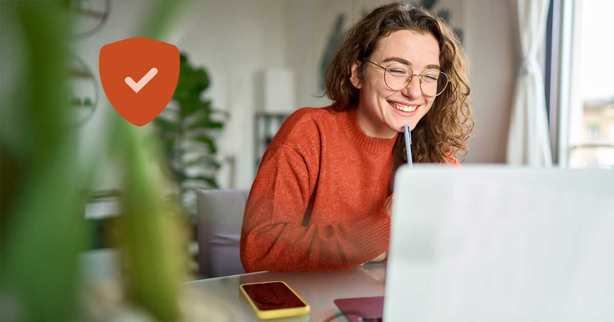 Junge Frau sitzt am Tisch und schaut auf Laptop