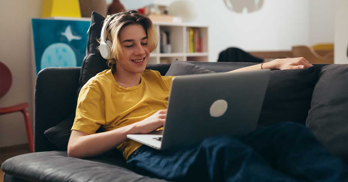 Teenager liegt auf Sofa mit Laptop auf dem Schoß